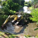 Excavator on a barge in a canal removing trees