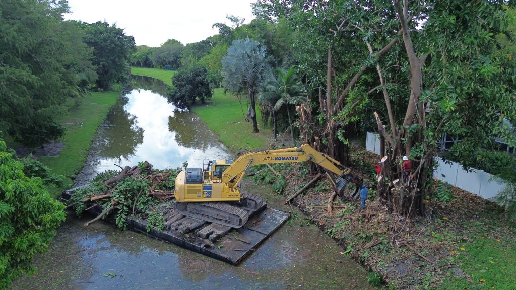 Excavator on a barge in a canal removing trees from bank