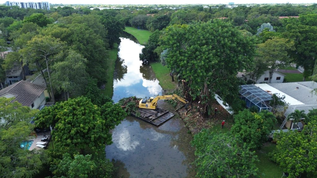 Excavator on a barge in a canal removing trees from the shore